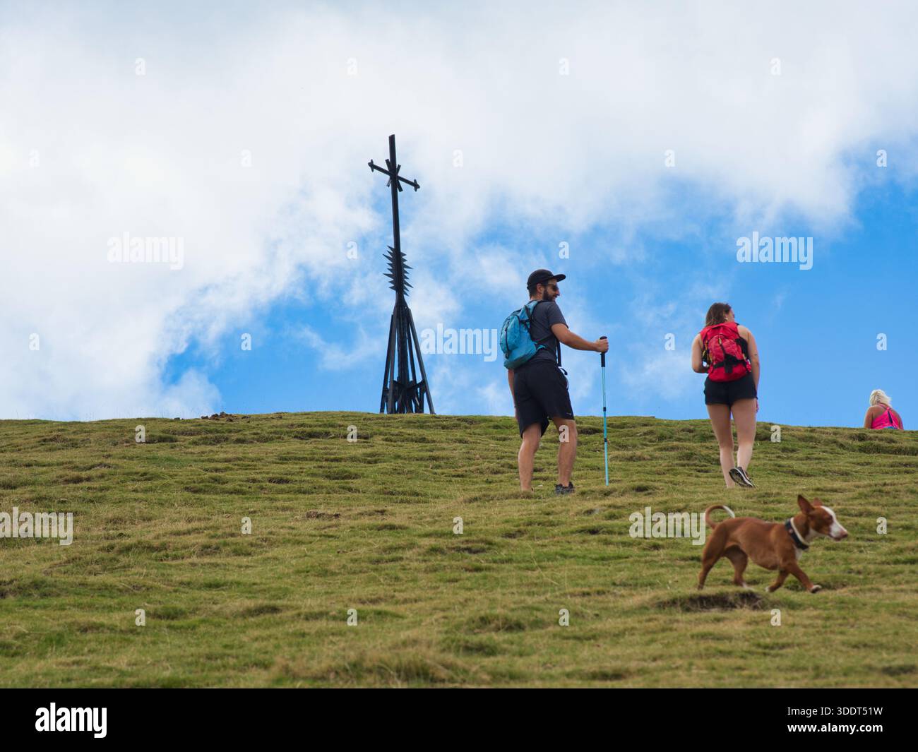 Otxandio-Autonomous Community of the Basque Country-Spain-September 6, 2022,Hikers ascend a steep, grassy hillside accompanied by a dog toward a large Stock Photo