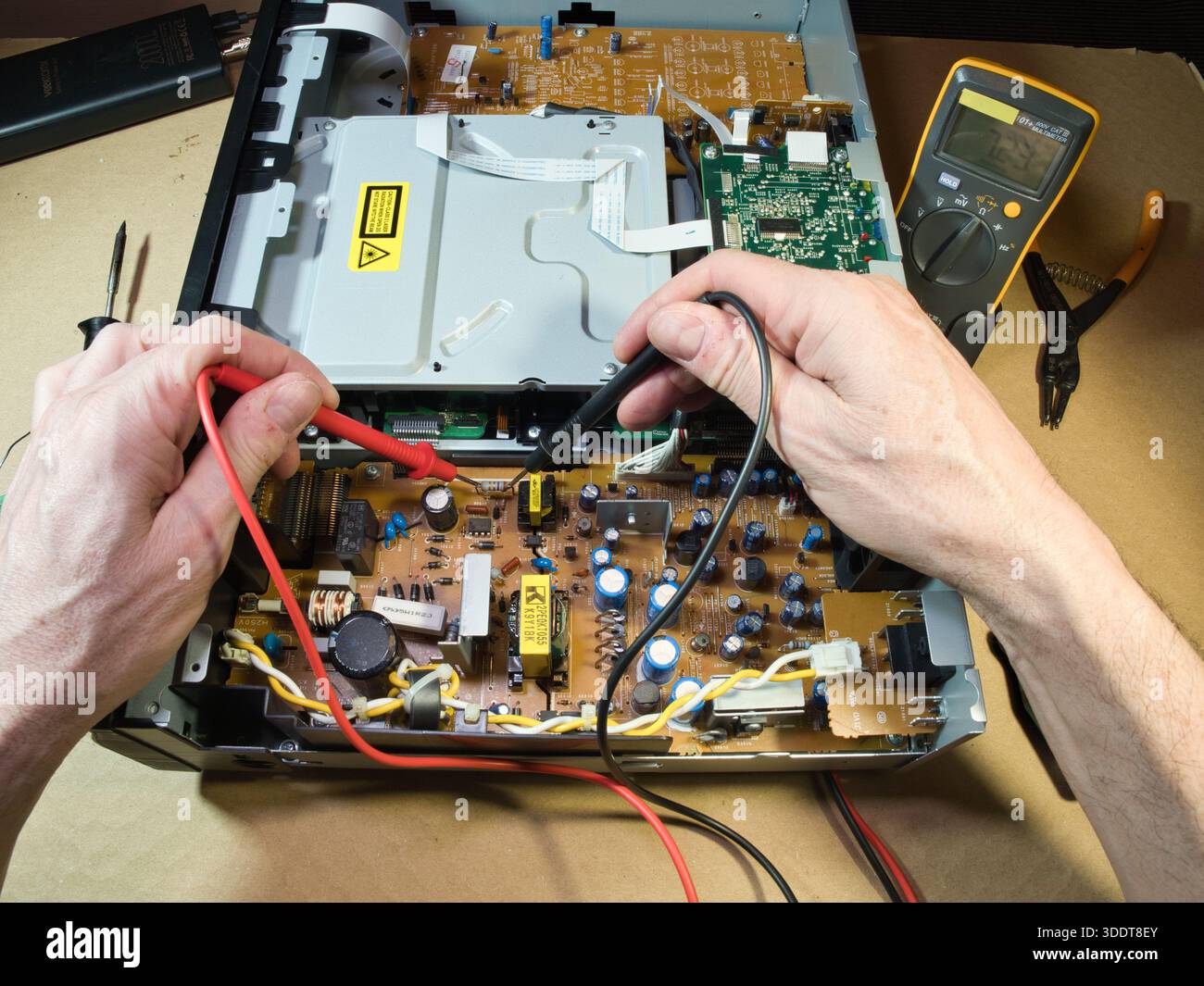 Hands Testing Electronic Circuit Board with Multimeter; Close-up of technician's hands using a multimeter to diagnose or repair complex electronic cir Stock Photo
