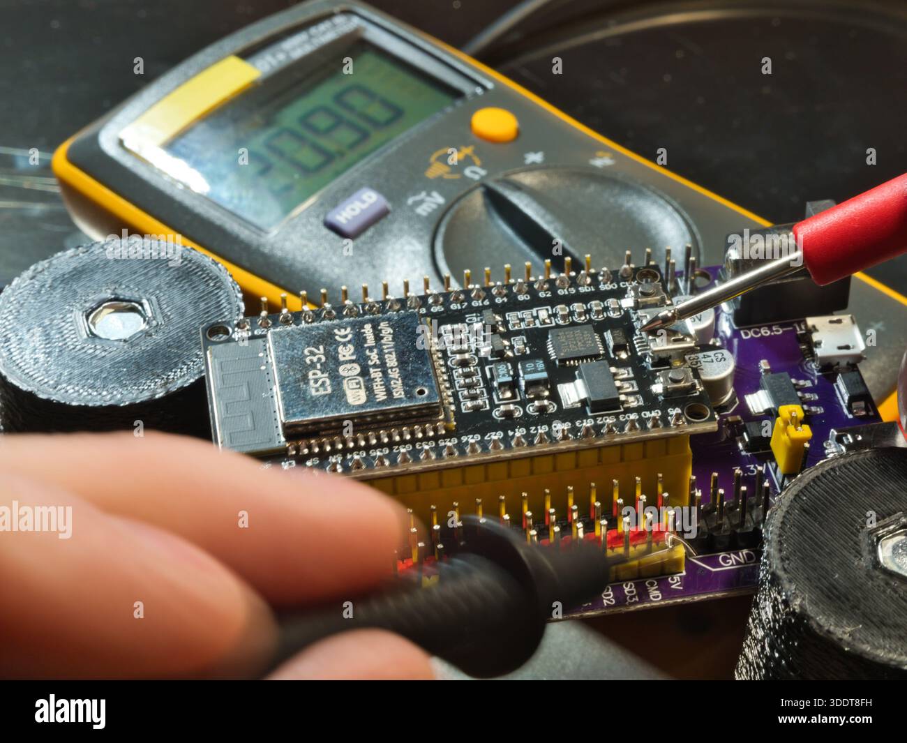 Engineer testing microcontroller board.; Close-up of an engineer testing voltage on a modern microcontroller development board (PCB) using a digital m Stock Photo