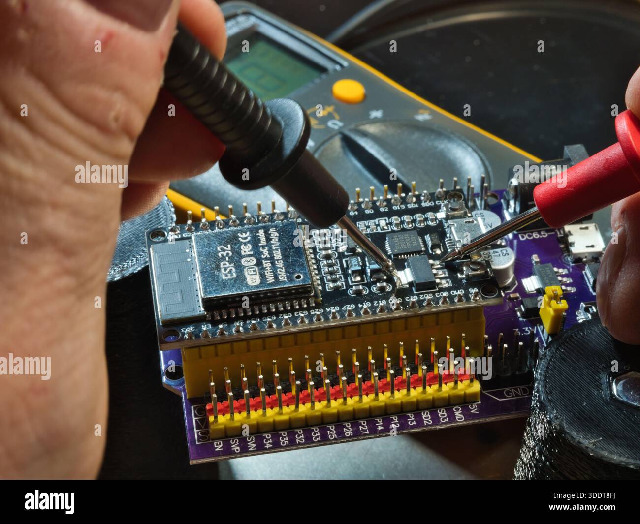 Engineer testing microcontroller board.; Close-up of an engineer testing voltage on a modern microcontroller development board (PCB) using a digital m Stock Photo