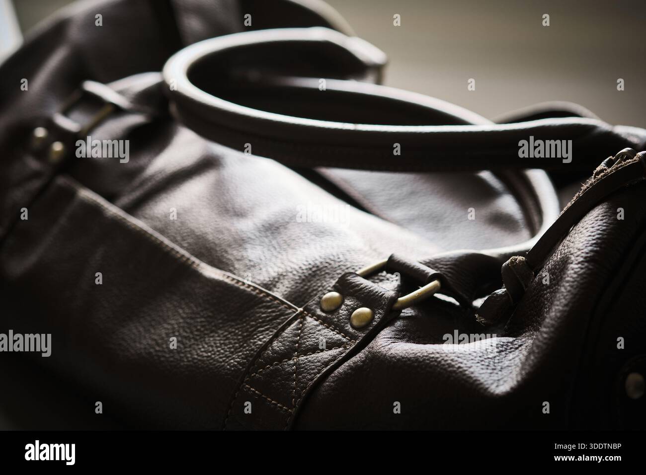 Close-up view of dark leather bag focusing on handle, strap attachment, and metal hardware. Natural leather texture, stitching, craftsmanship, premium Stock Photo
