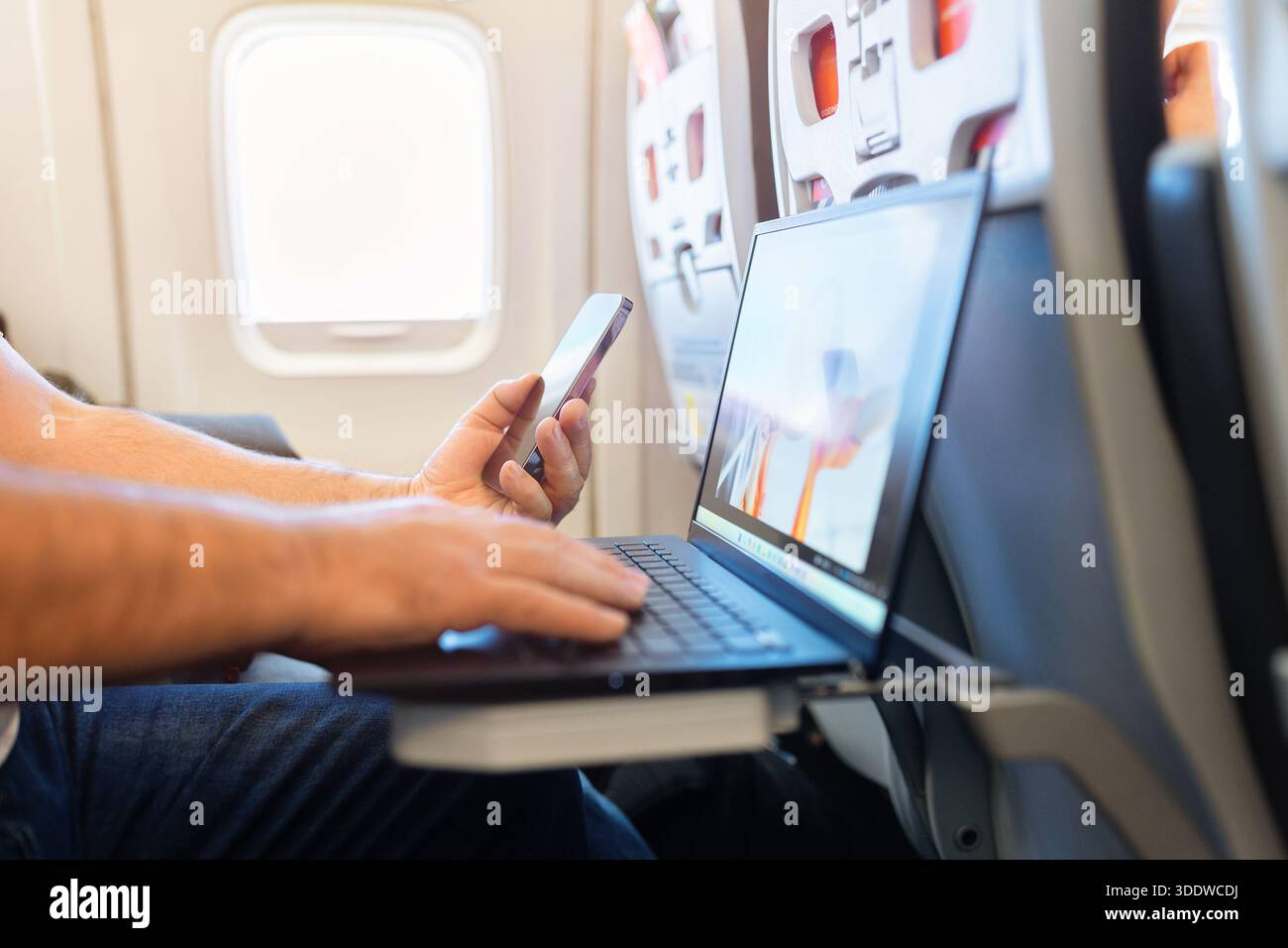 Passenger using smartphone and laptop simultaneously during airplane flight Stock Photo
