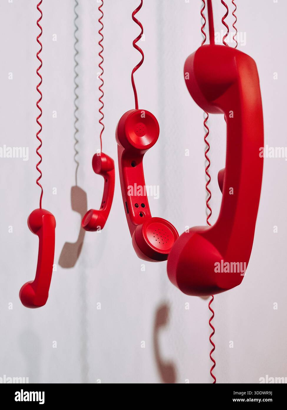 Close-up of red retro handsets on coiled cords. A vertical shot of several bright red vintage telephone receivers hanging by their spiral cords. Stock Photo