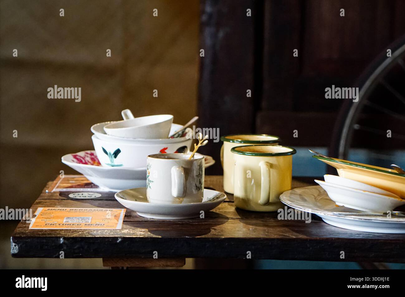 Assorted vintage enamelware and ceramic dishes with food remnants on a rustic wooden cafe table after dining. Stock Photo