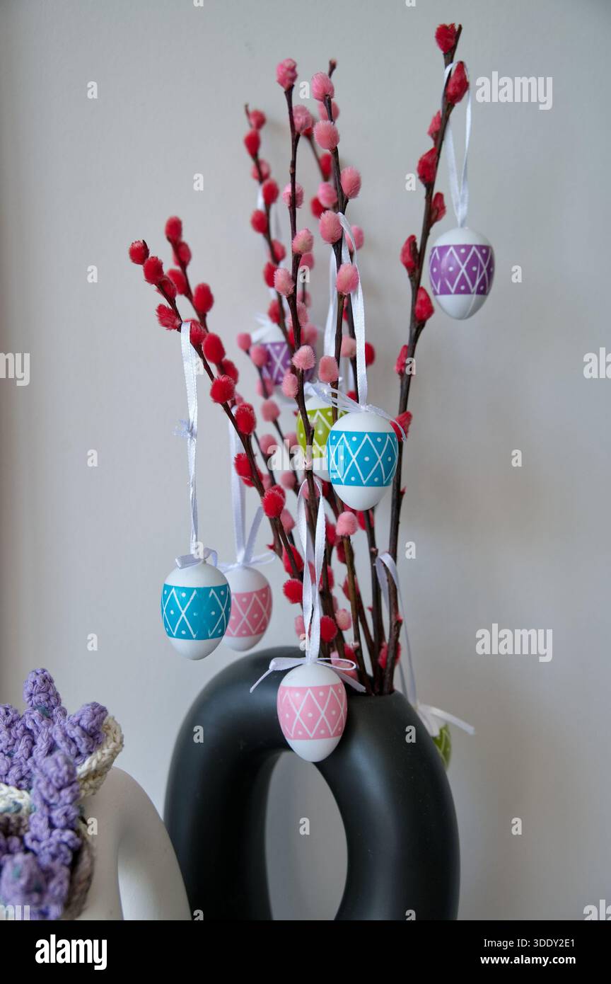 Vase with branch and Easter eggs against white wall Stock Photo
