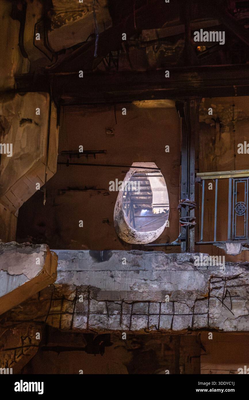 Ruined industrial interior with oval wall opening revealing structural ...