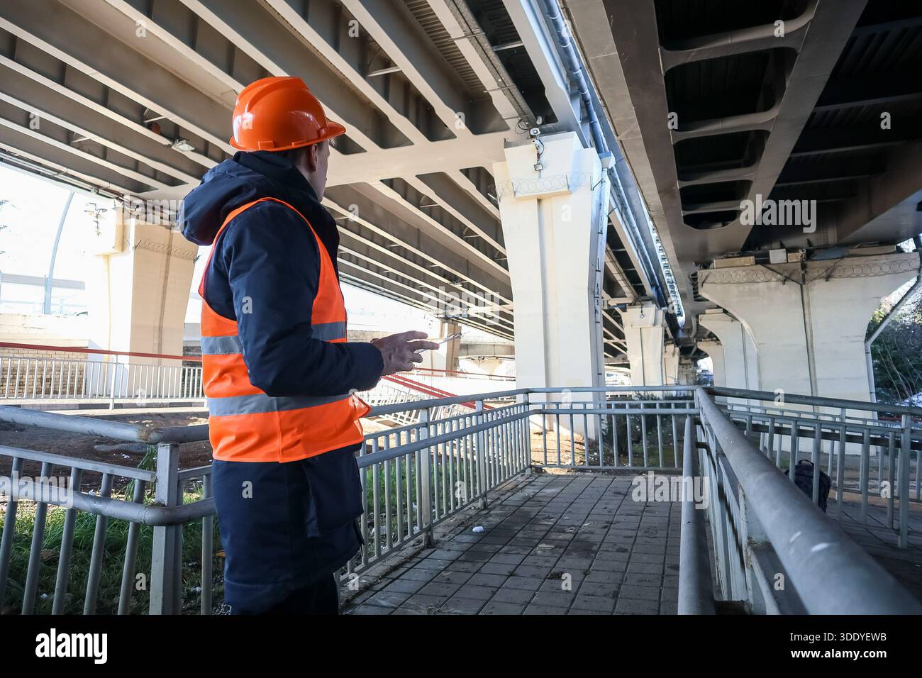 Side view of construction worker in hard hat pointing at concrete overpass elements. Stock Photo