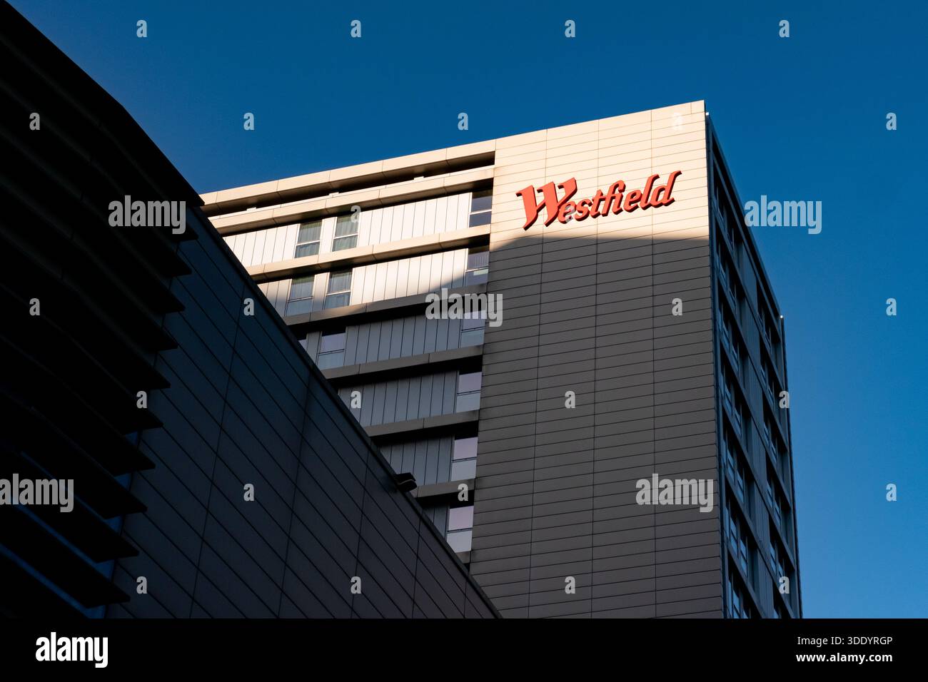 Looking up at Westfield shopping centre sign on the Premier Inn Hotel, Stratford London. The sun casts a shadow on the building with the sign in light Stock Photo