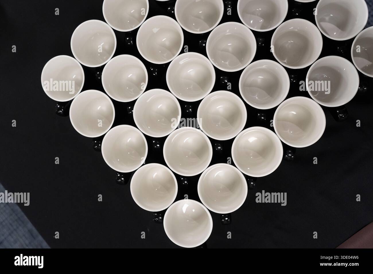 White cups arranged in a diamond pattern on a black surface Stock Photo