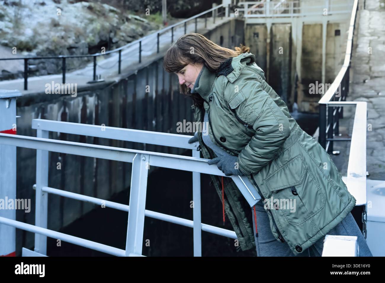 Slow pace lifestyle moment for adult woman leaning over a railing, observing water below during daily walk, expressing reflective thinking, independen Stock Photo