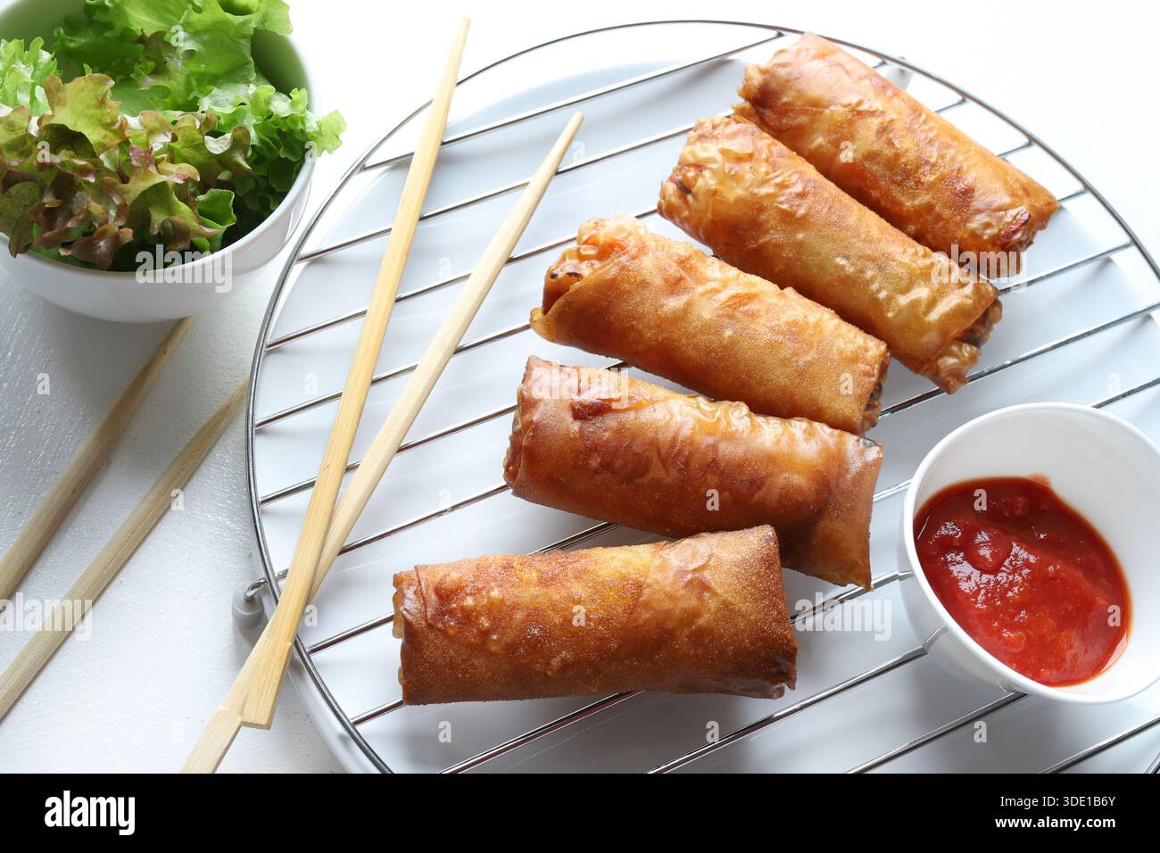 Crispy fried spring rolls (Chinese rolls) served with chopsticks, red sauce and fresh lettuce on a white background. Typical dish of Asian cuisine. Stock Photo