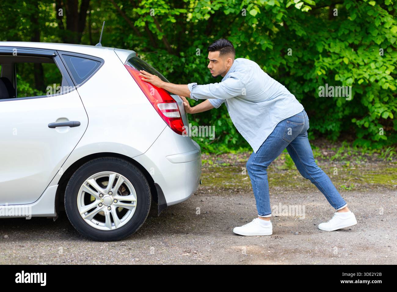 Arab guy pushing broken car, side view Stock Photo
