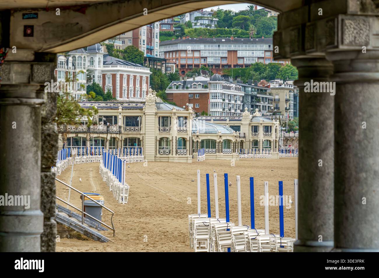 La Concha Beach Viewed Through Stone Columns, Folded Blue Umbrellas, San Sebastian, Donostia, Basque Country, Spain Stock Photo