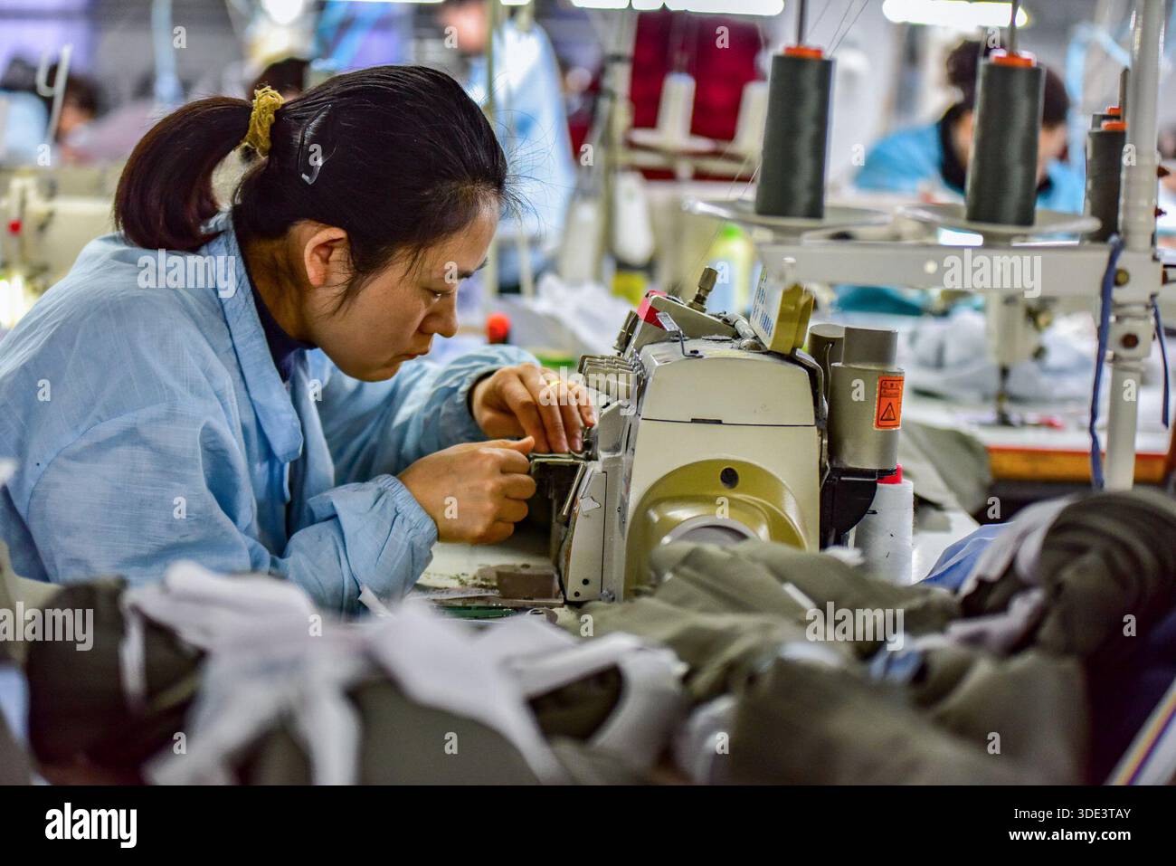 A female worker adjusts parts of a sewing machine while working on ...