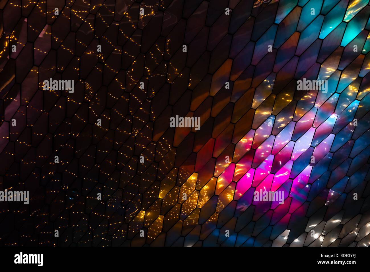 abstract, geometric wall made of hexagonal, glass-like tiles. The tiles reflect colorful lights creating a vibrant, shimmering effect. The overall tex Stock Photo