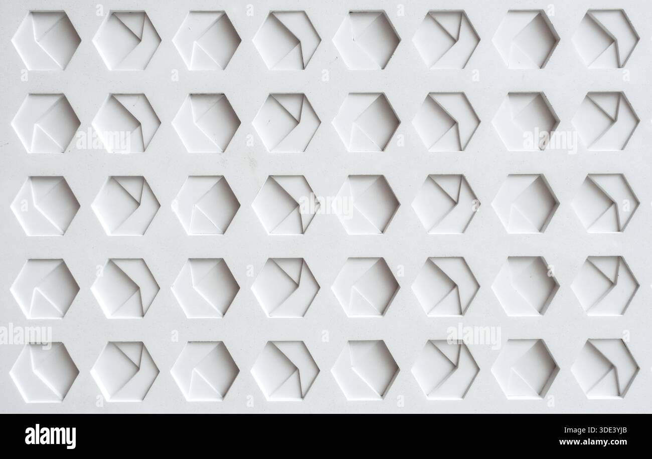a white, textured surface featuring a grid of hexagonal indentations. Each hexagon has a three-dimensional, geometric design with internal triangular Stock Photo