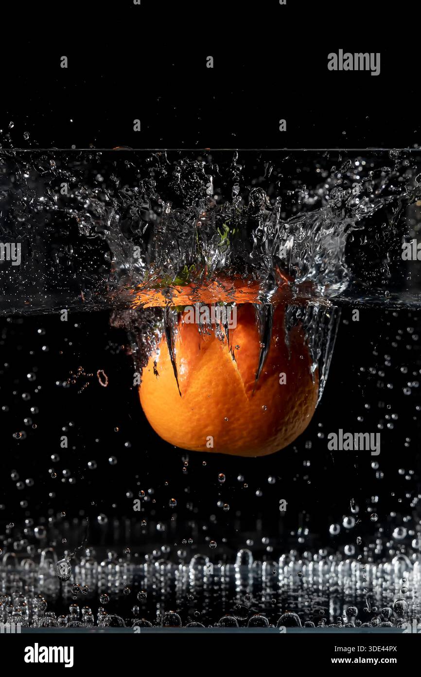 A mandarin falls into a container full of water, raising a large splash Stock Photo