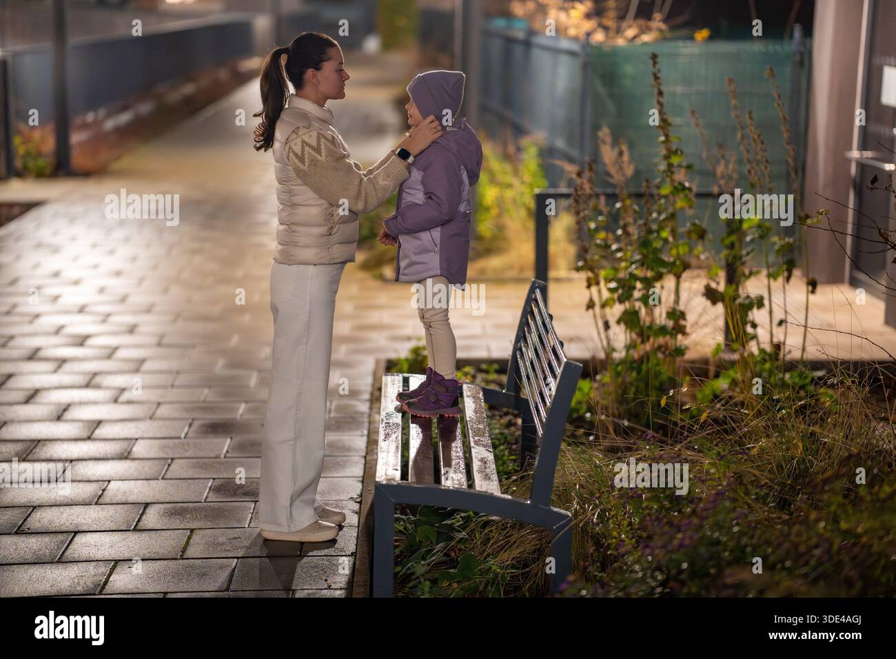 Mother helps child zip up jacket outside on cold evening. Parenting care and warmth. Stock Photo