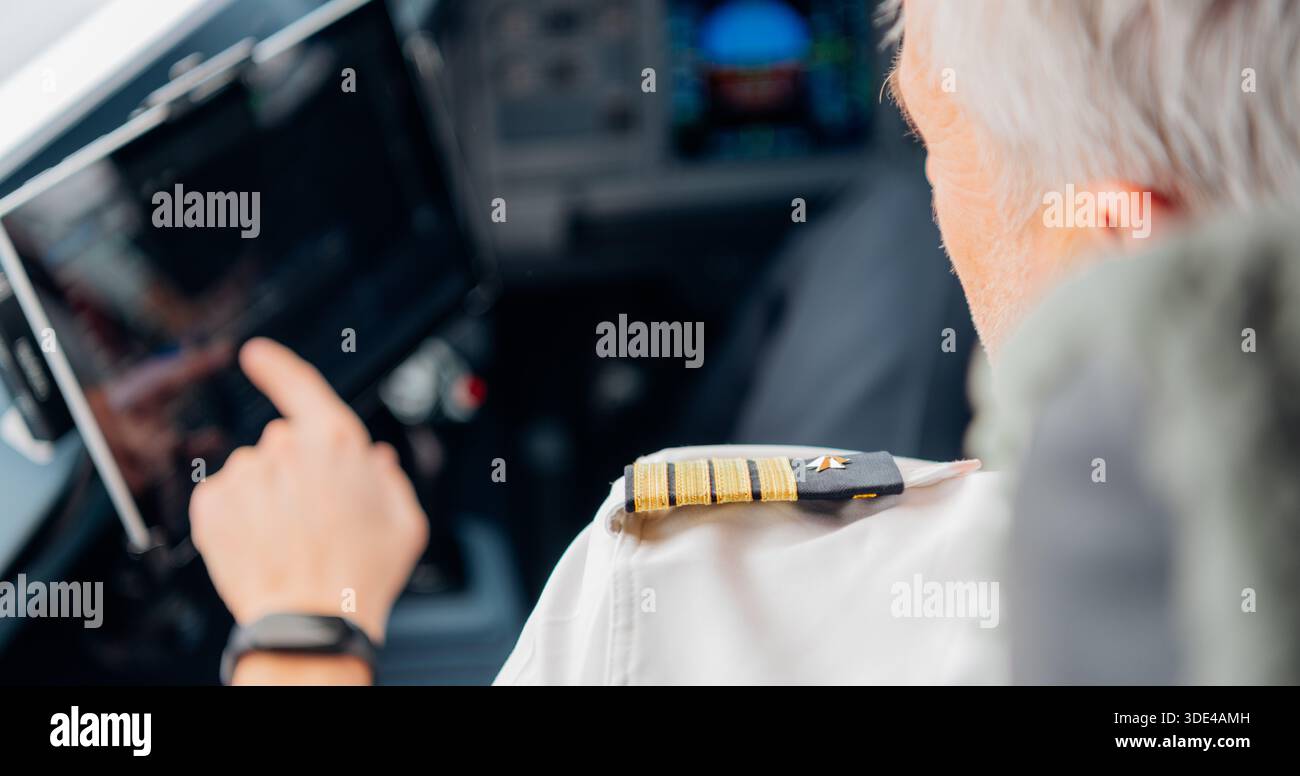 Senior male pilot using digital touchscreen in airplane cockpit Stock Photo