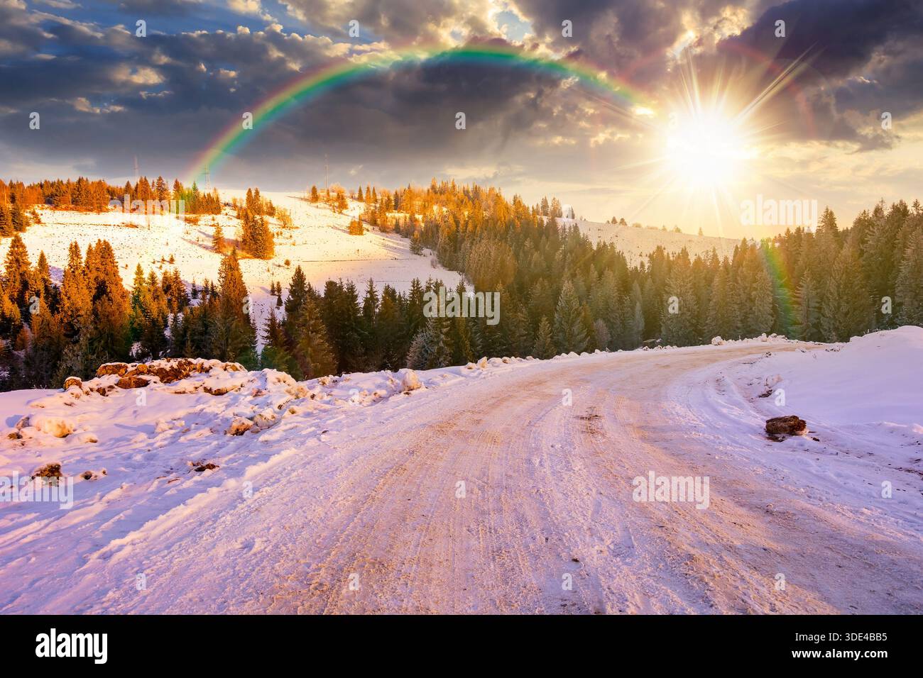 winter landscape with snow covered country road winding through fir forest in mountains at sunset. alpine countryside of in evening light. timeless no Stock Photo
