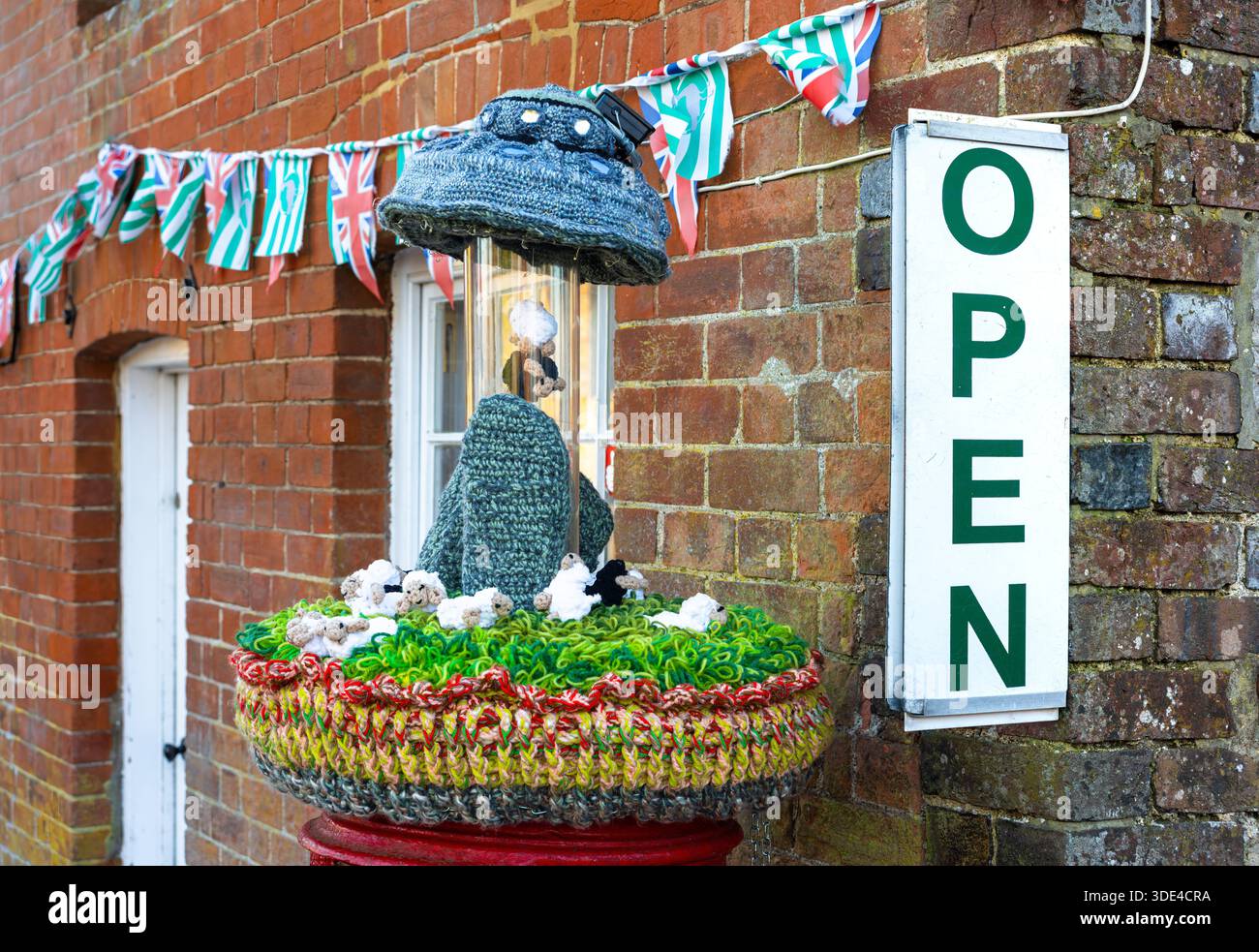A charming storefront in Avebury, England, with a knitted display featuring a hat and decorative elements, surrounded by colorful bunting. A sign read Stock Photo