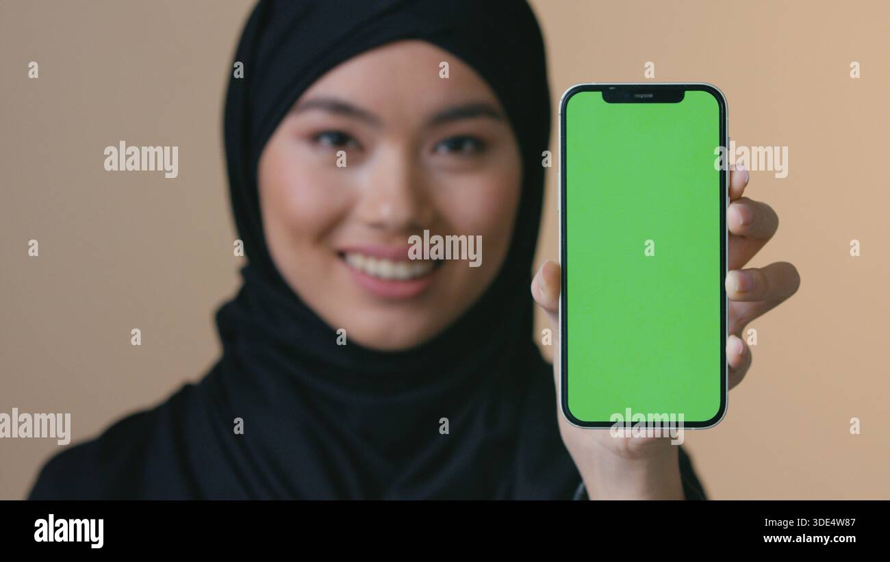 Smiling Asian Muslim woman in black hijab holding smartphone green ...