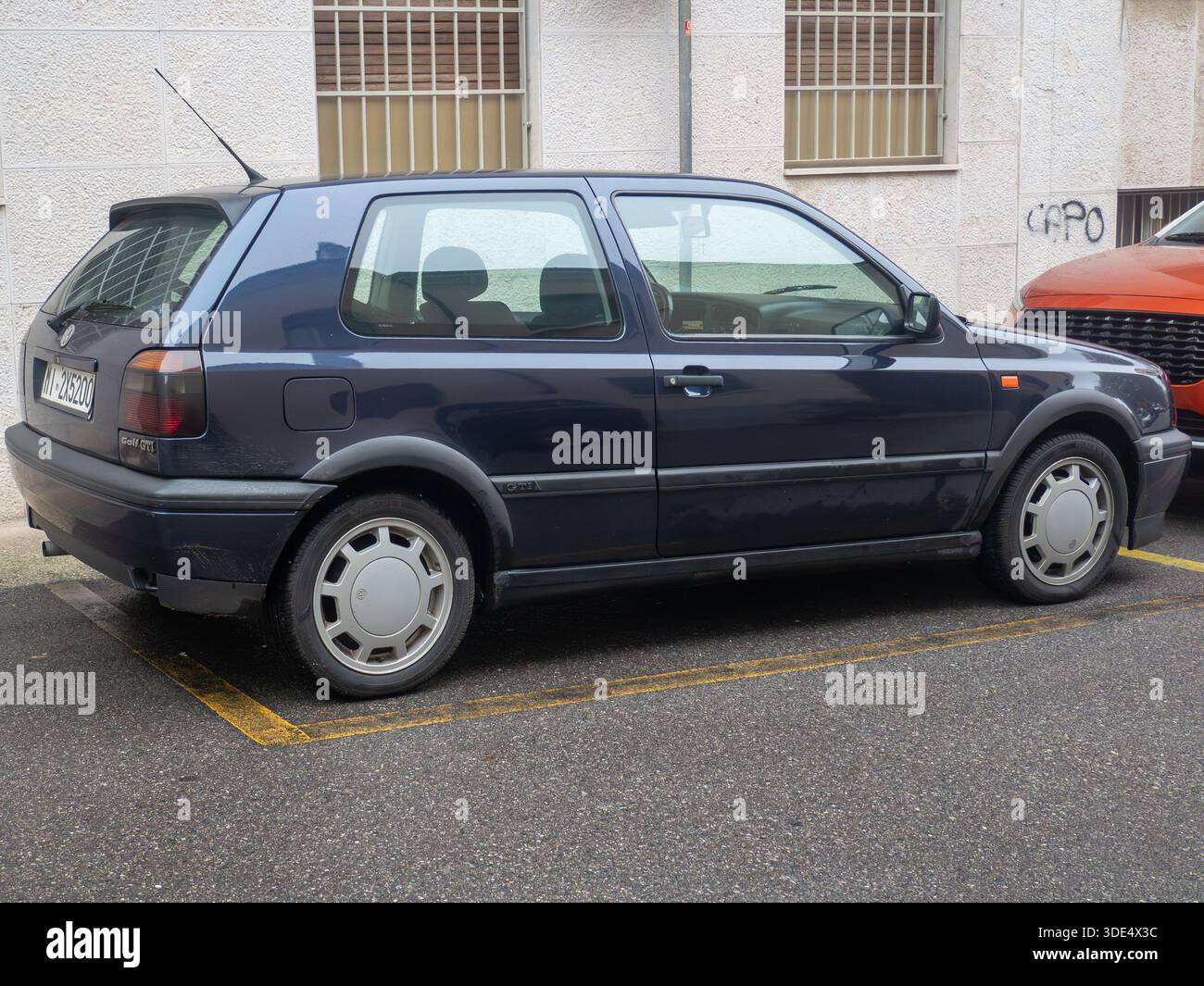 A classic dark blue Volkswagen Golf GTI from the 1990s is parked in a ...