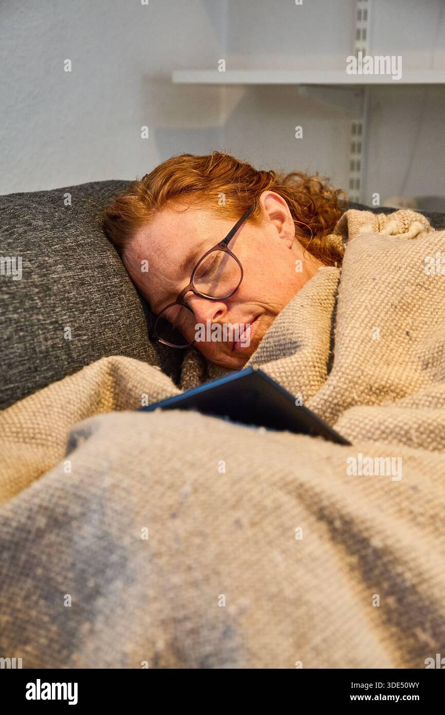 A woman sleeping on a couch holding a tablet Stock Photo