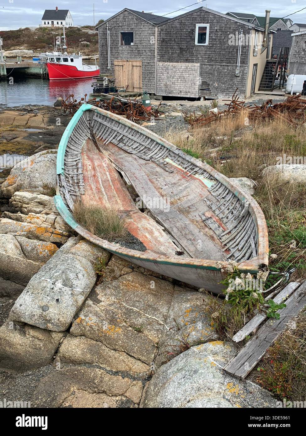 A weathered wooden fishing dory rests on granite rocks near fishing sheds at Peggy’s Cove, Nova Scotia, Canada. - Smartphone Captured Stock Image