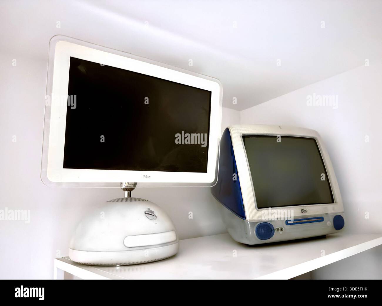 Two vintage Apple iMac G3 and iMac G4 desktop computers on a white shelf in a minimalist interior setting - Smartphone Captured Stock Image