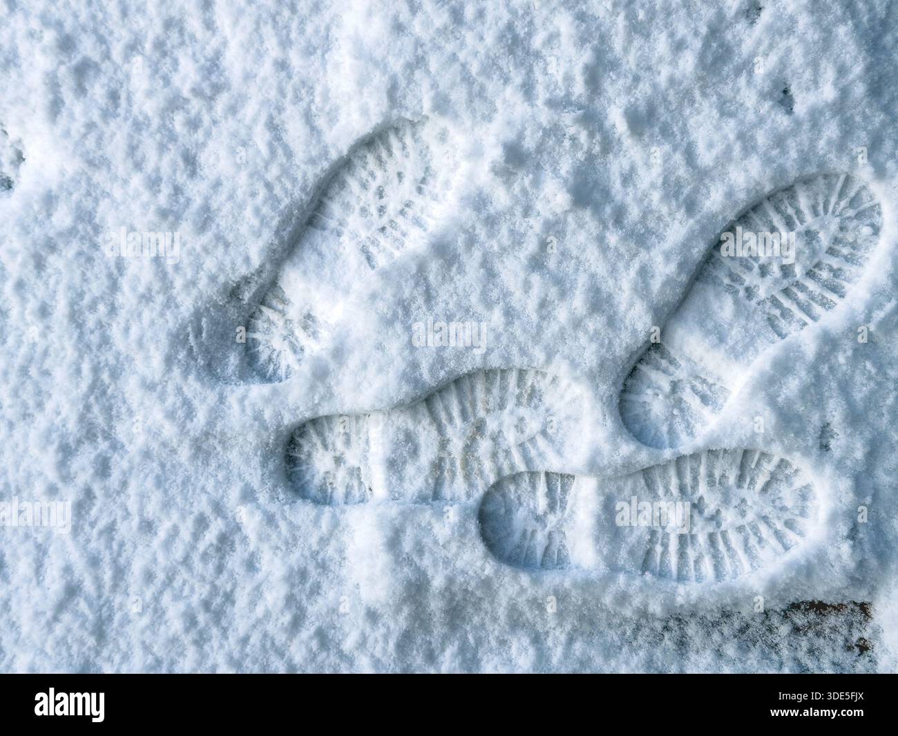 Multiple boot prints in freshly fallen snow showing deep tread patterns and overlapping footsteps on a cold winter frozen surface - Smartphone Captured Stock Image