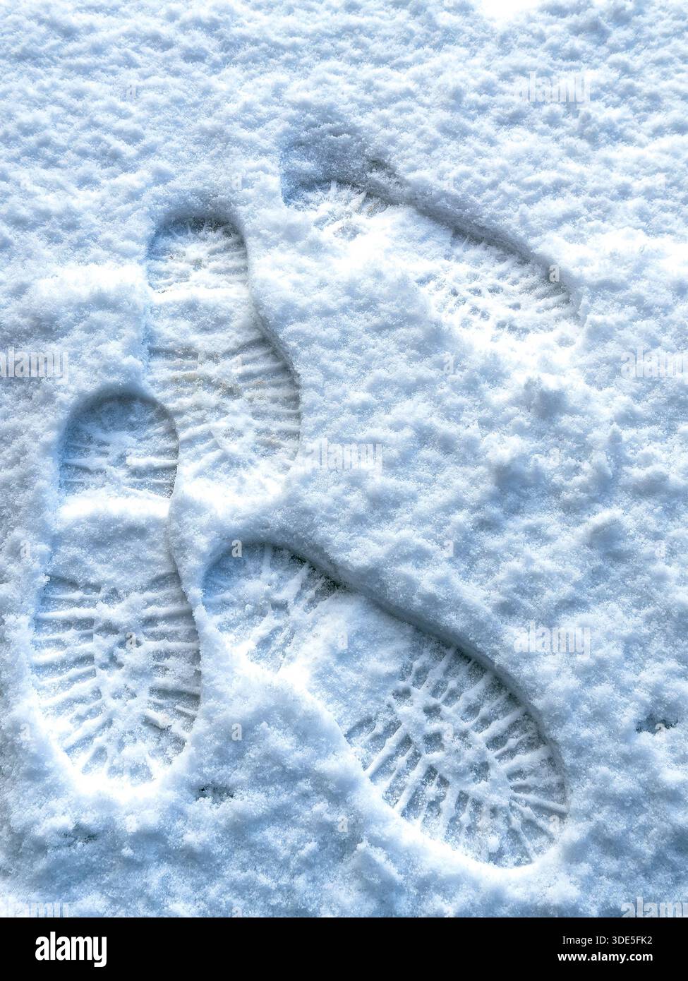 Multiple boot prints in freshly fallen snow showing deep tread patterns and overlapping footsteps on a cold winter frozen surface - Smartphone Captured Stock Image