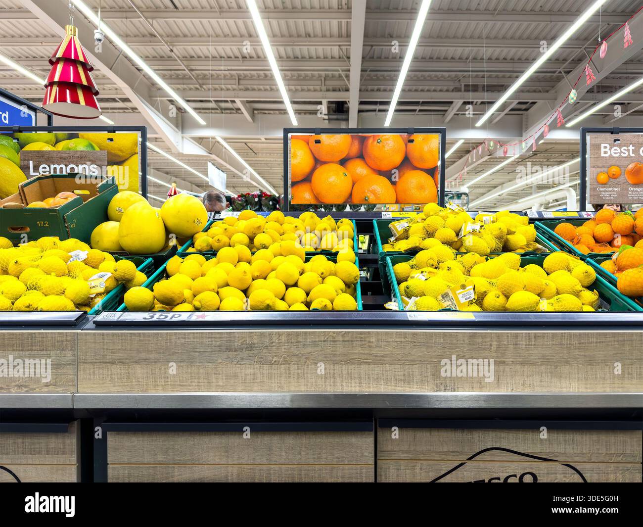 Stacked trays of yellow citrus fruits including lemons and melons displayed under fluorescent lighting in a tesco supermarket fruit & veg section uk - Smartphone Captured Stock Image