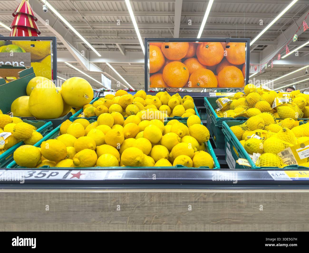 Stacked trays of yellow citrus fruits including lemons and melons displayed under fluorescent lighting in a tesco supermarket fruit & veg section uk - Smartphone Captured Stock Image