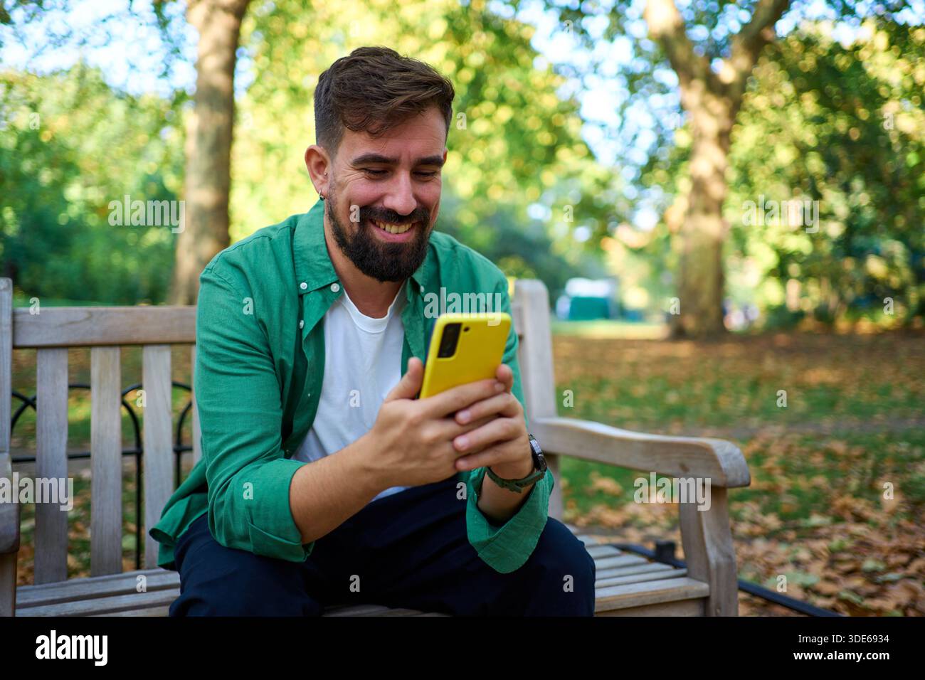 Happy man smiling using yellow smartphone in park Stock Photo