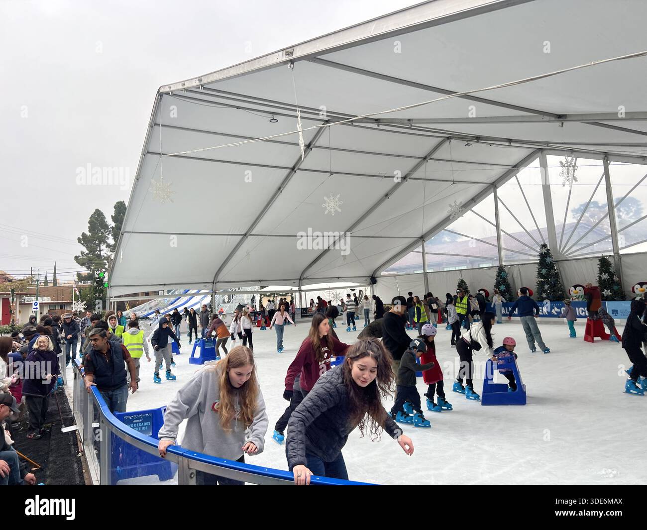 Crowd of people ice skating at outdoor seasonal rink under large tent ...
