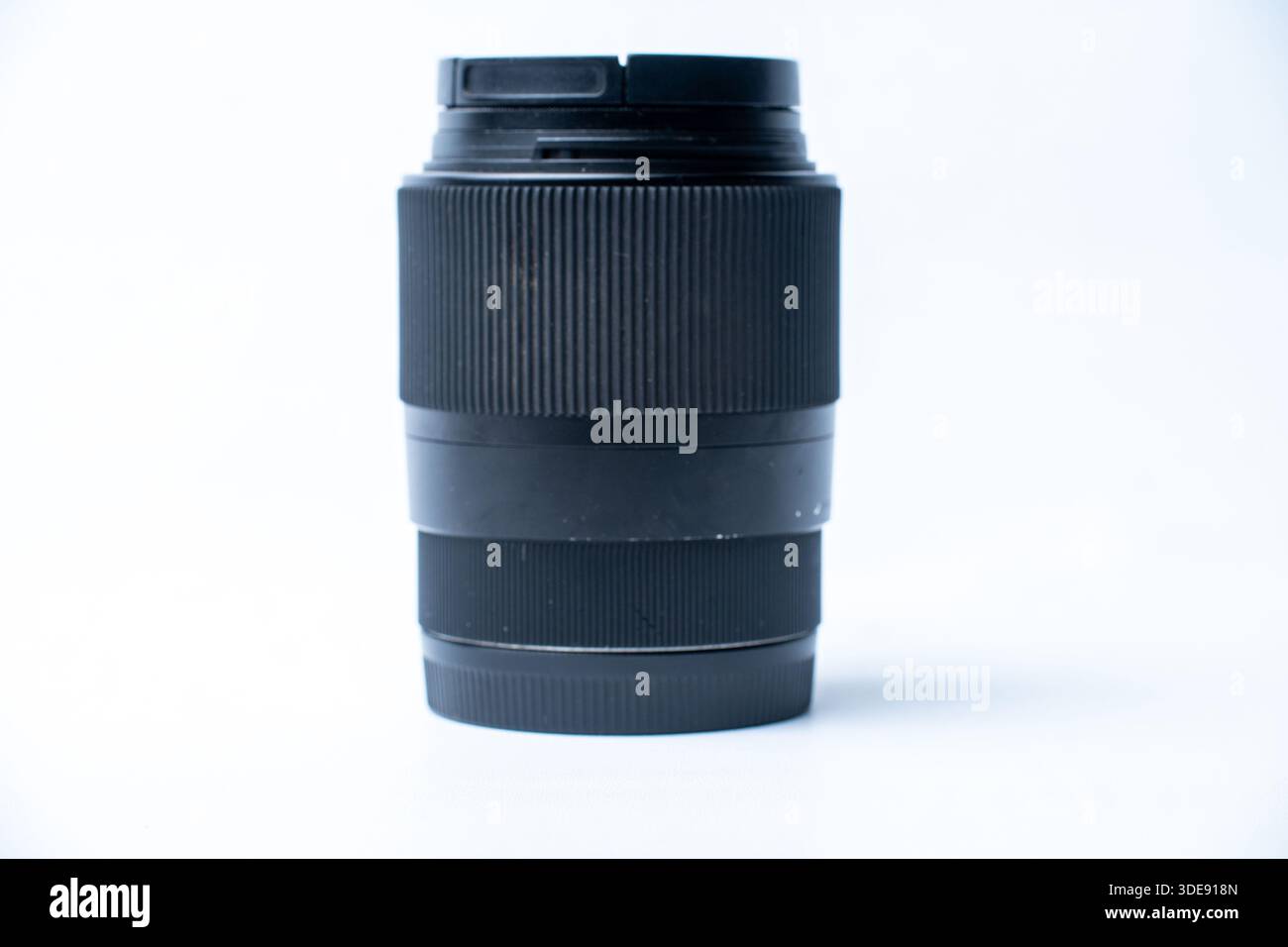 A sleek black camera lens standing upright on a clean white surface. Ideal for photography gear reviews, equipment sales, and technology concepts. Stock Photo
