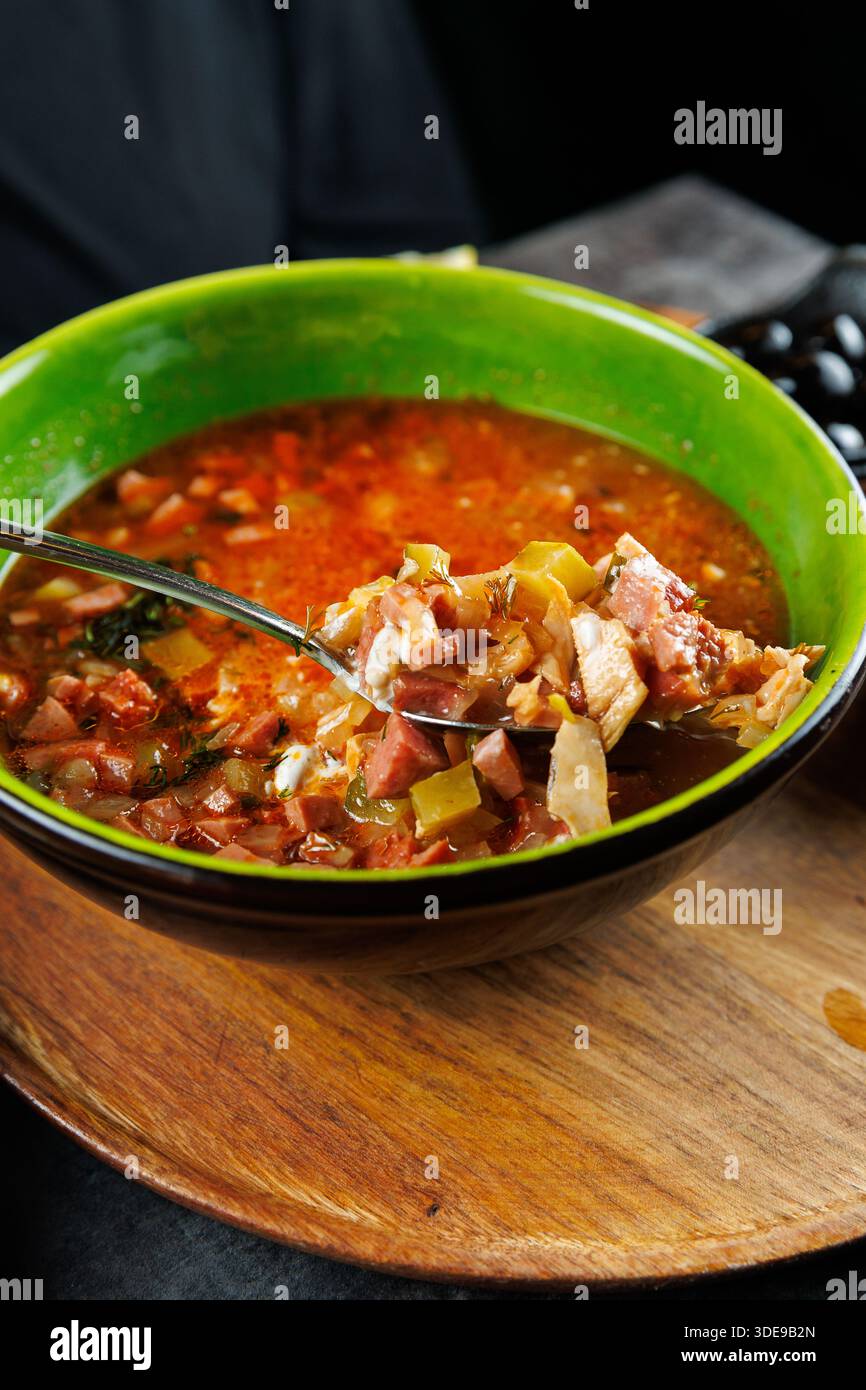 Delicious soup is served in a green bowl with a spoon filled with hearty ingredients. The dish showcases flavors from Ukrainian and other cuisines, in Stock Photo