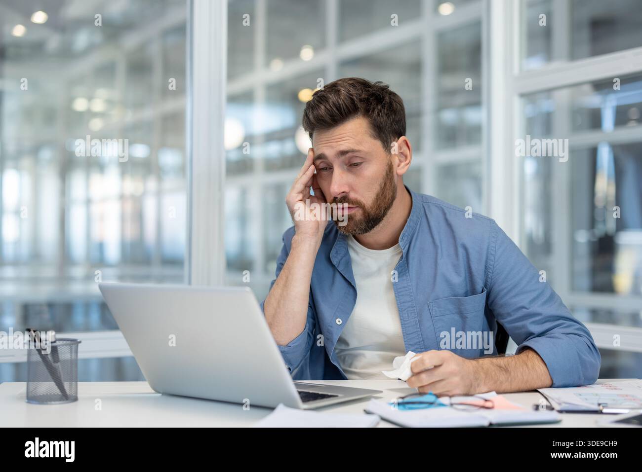 Overworked businessman sitting at an office desk, holding his head and ...