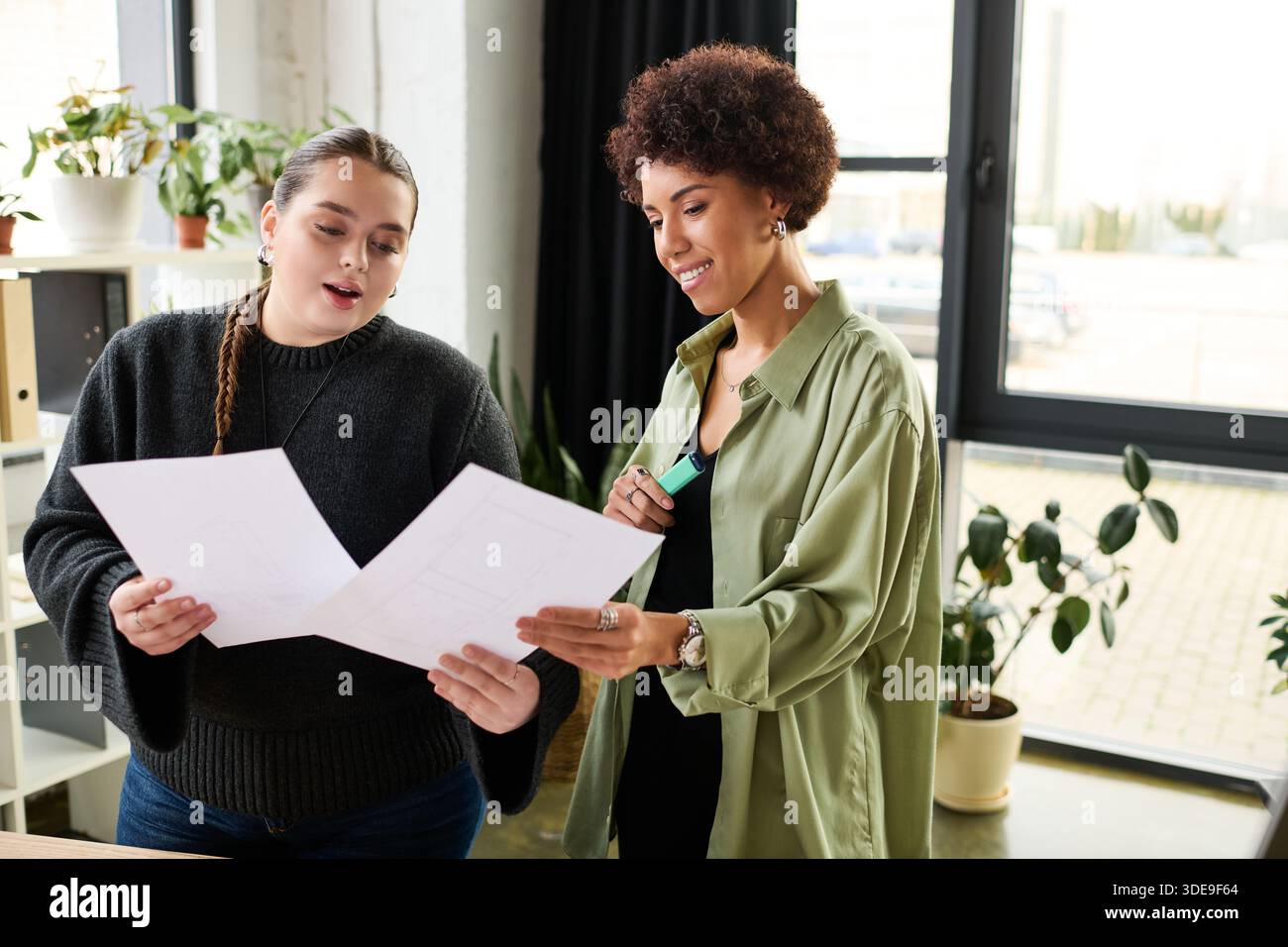 Two female managers discuss plans while reviewing documents in a bright, stylish workspace. Stock Photo