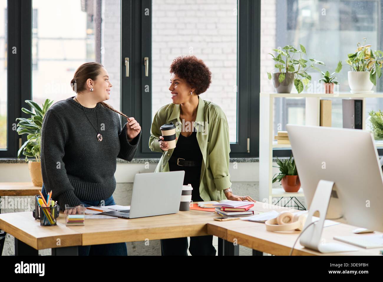Two female managers share ideas and laughter while collaborating in a bright office. Stock Photo