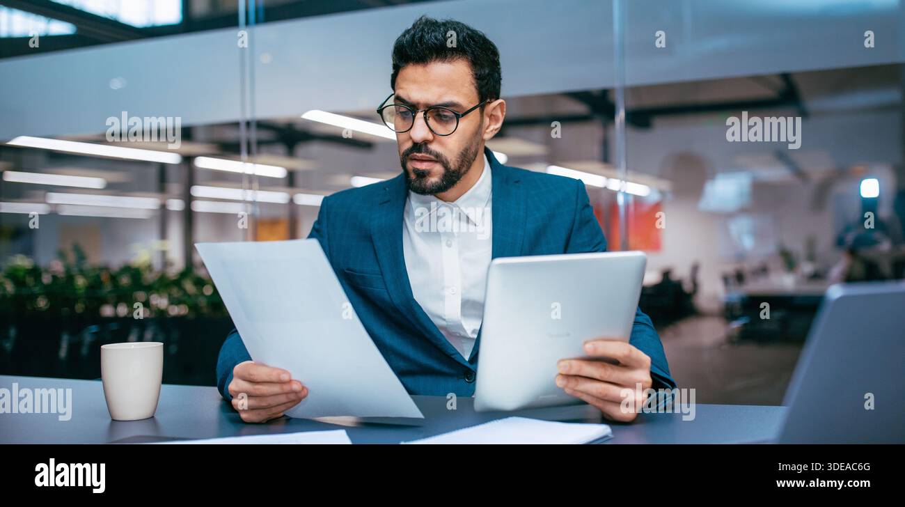 Businessman Reads Reports and Checks Tablet in Modern Office Setting During Work Hours Stock Photo
