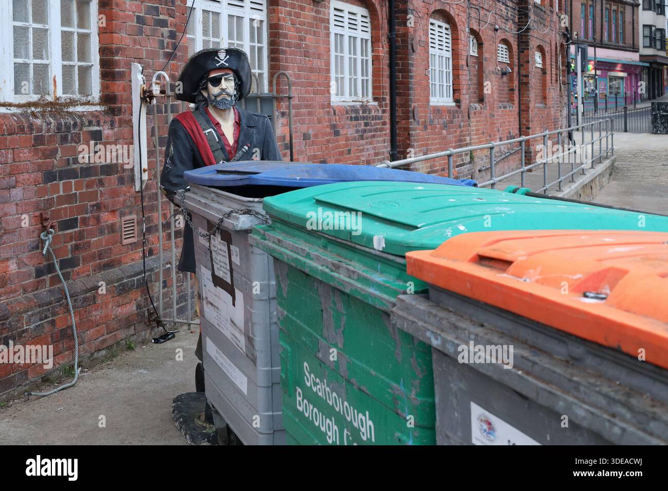 Life-sized pirate statue appears to push a row of commercial wheelie bins in Scarborough, North Yorkshire, England, UK Stock Photo