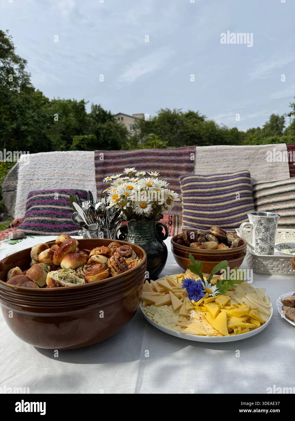 Rustic outdoor table with homemade food, floral ceramics and daisies set for garden gathering - Smartphone Captured Stock Image