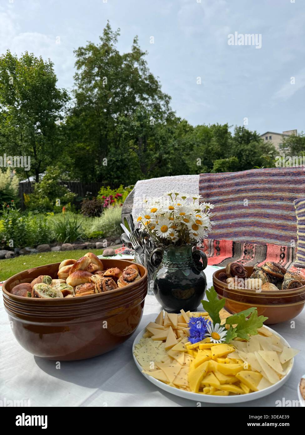 Rustic outdoor table with homemade food, floral ceramics and daisies set for garden gathering - Smartphone Captured Stock Image