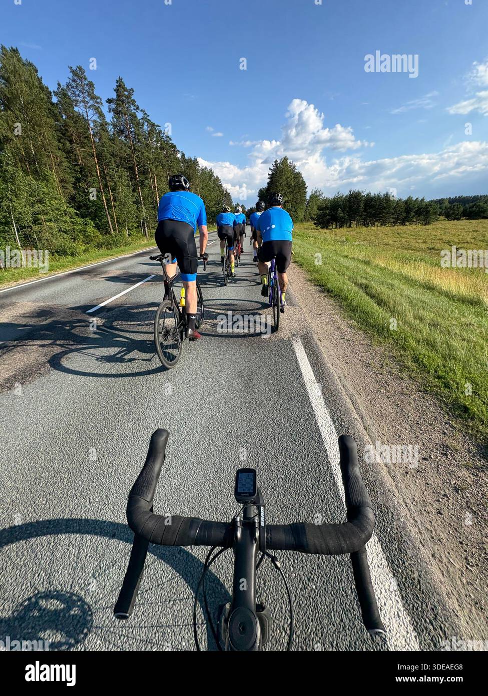 Cyclists riding through scenic countryside on paved road, viewed from handlebar perspective under blue sky - Smartphone Captured Stock Image