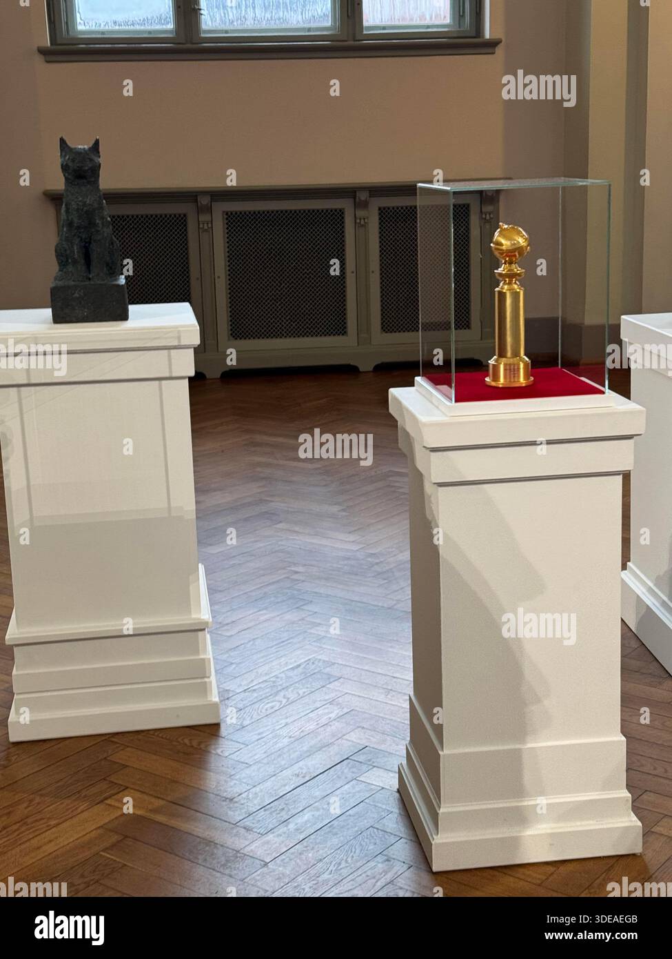 Golden Globe trophy and Flow cat sculpture displayed on pedestals in elegant interior with classical architecture - Smartphone Captured Stock Image
