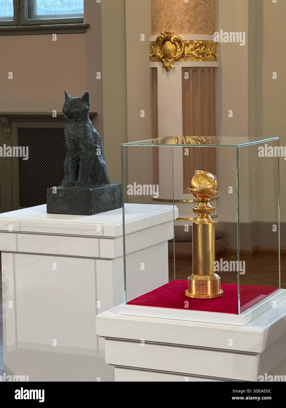 Golden Globe trophy and Flow cat sculpture displayed on pedestals in elegant interior with classical architecture - Smartphone Captured Stock Image