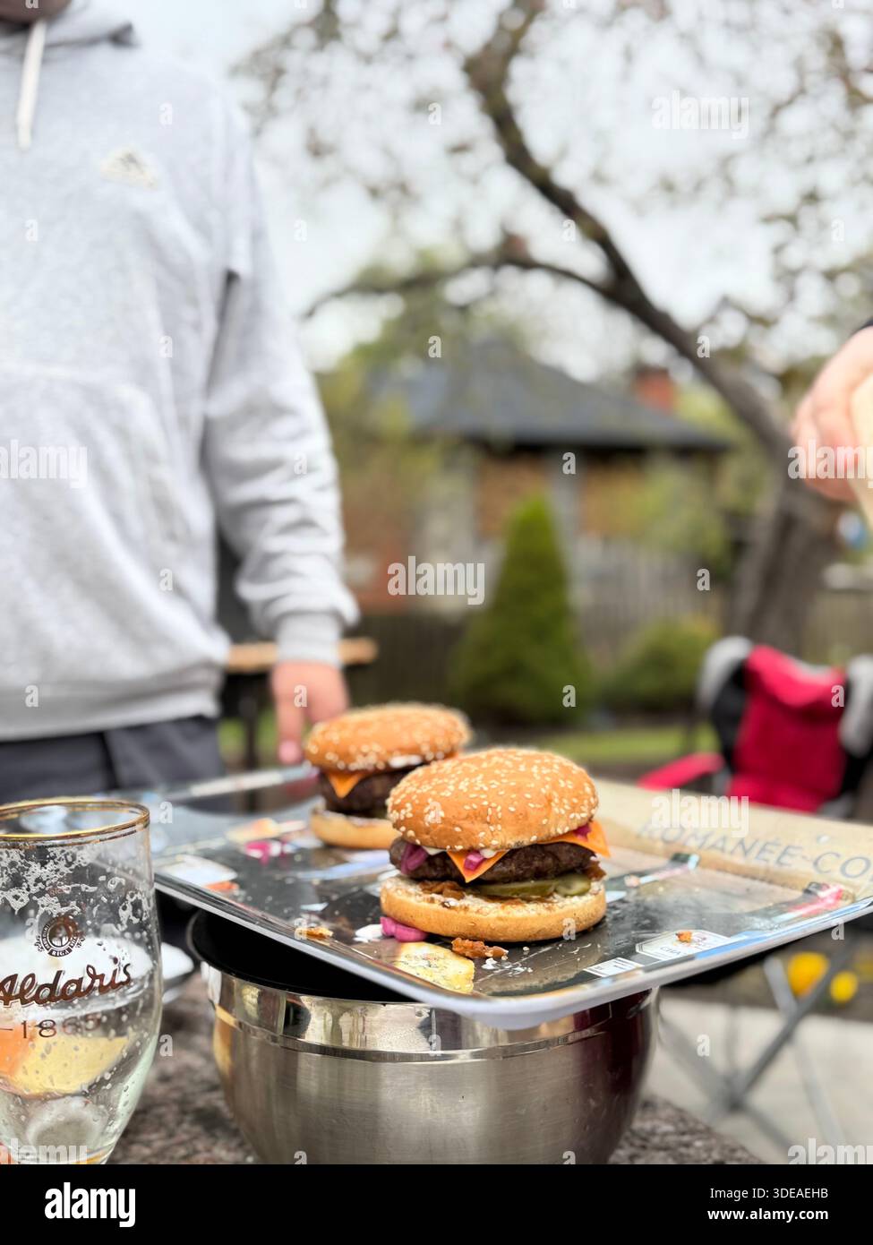 Homemade cheeseburgers served outdoors on metal tray during casual gathering in springtime garden - Smartphone Captured Stock Image