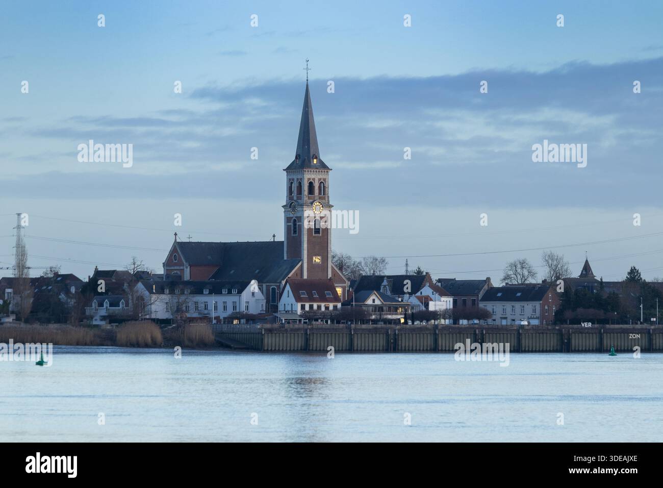 Winter skyline view of Sint Amands, Antwerp Province, Belgium, looking across the Scheldt river during blue hour. Sint Amandus church is dominant in t - Stock Image